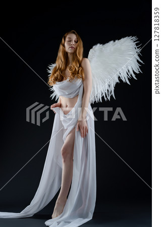 Red-haired woman with angel wings poses nude with body art in studio setting Red-haired woman with angel wings poses nude with body art in studio setting 127818359