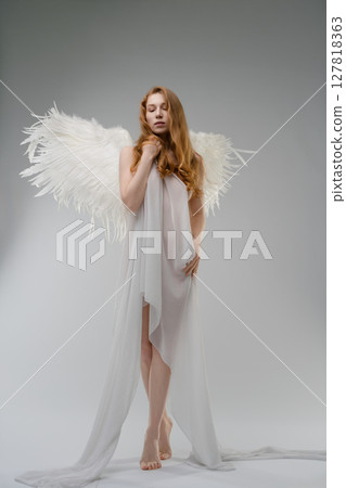 Red naked woman poses with angel wings and body art in studio setting 127818363