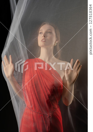 Woman posing gracefully in a red dress with sheer fabric in a dramatic studio setting evoking strong emotion Woman posing gracefully in a red dress with sheer fabric in a dramatic studio setting evoking strong emotion 127818364
