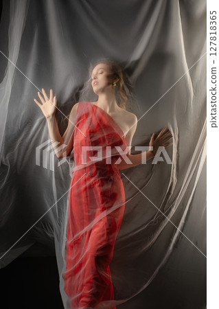 Woman posing gracefully in a studio setting, expressing deep emotion while draped in flowing fabric 127818365