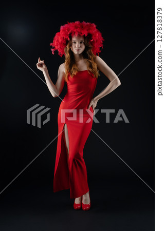 Woman expressing confidence and emotion while posing in a studio setting with vibrant red attire and a feathered headpiece 127818379