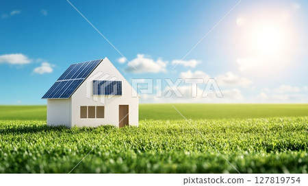 Small model house with solar panels standing in a green field under a blue sky with shining sun representing sustainable living and eco friendly energy generation 127819754