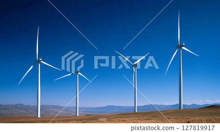 Four wind turbines are actively generating renewable energy on a clear day, contributing to a sustainable future with clean power against a backdrop of distant mountains and blue sky 127819917