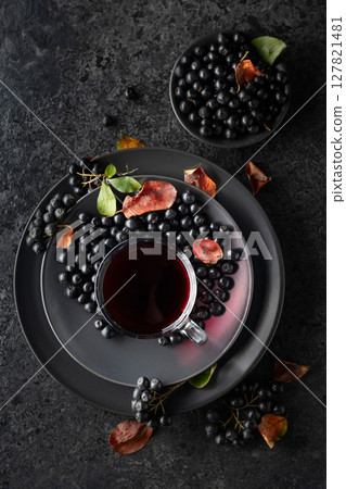 Black chokeberry drink and fresh berries on a black stone table. Black chokeberry drink and fresh berries on a black stone table. 127821481
