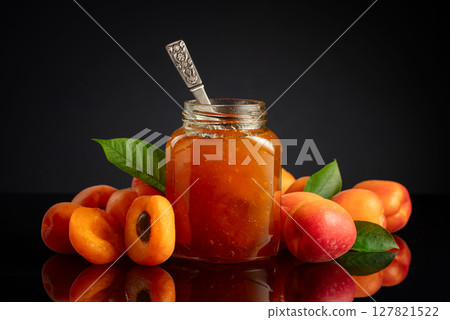 Apricot jam in glass jar and fresh fruits on a black reflective background. Apricot jam in glass jar and fresh fruits on a black reflective background. 127821522