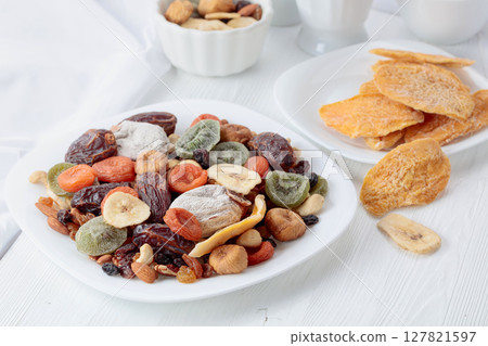 Mix of dried tropical fruits, nuts, and raisins on a white table. Mix of dried tropical fruits, nuts, and raisins on a white table. 127821597
