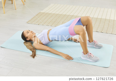 Athletic girl doing buttocks exercises with fitness band at home, close-up Athletic girl doing buttocks exercises with fitness band at home, close-up 127821726