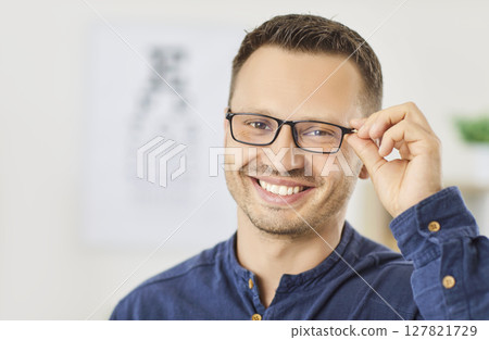 Smiling man choosing and trying on glasses in ophthalmology clinic, optical store to improve vision. Smiling man choosing and trying on glasses in ophthalmology clinic, optical store to improve vision. 127821729