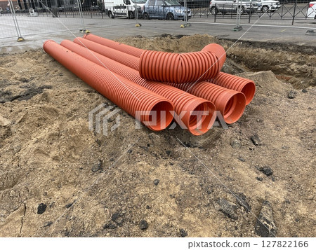A construction site with bright orange pipes, excavated materials, and equipment 127822166