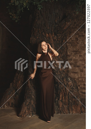 An Elegant and Graceful Woman Posing by a Beautiful Tree Background in a Sophisticated Dress An Elegant and Graceful Woman Posing by a Beautiful Tree Background in a Sophisticated Dress 127822897