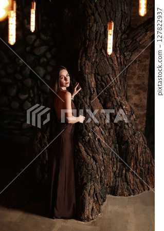 An Elegant Woman is Posing Gracefully by a Textured Wall While Wearing a Brown Dress 127822937