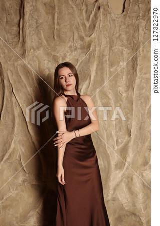 An Elegant Woman Gracefully Posing in a Beautiful Brown Dress Against a Textured Background An Elegant Woman Gracefully Posing in a Beautiful Brown Dress Against a Textured Background 127822970