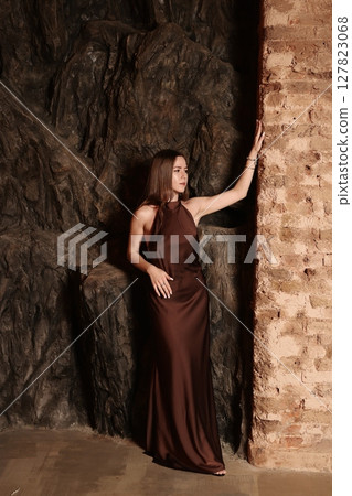 An Elegant Woman Posing Gracefully in a Luxury Brown Dress Set Against a Textured Wall An Elegant Woman Posing Gracefully in a Luxury Brown Dress Set Against a Textured Wall 127823068