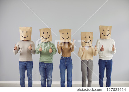 Faceless anonymous people standing in a row showing thumb up sign with paper bag on head with smile 127823634