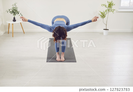 Sporty yogi woman working standing in Uttanasana with palms, hands wide open, head to knees Sporty yogi woman working standing in Uttanasana with palms, hands wide open, head to knees 127823783