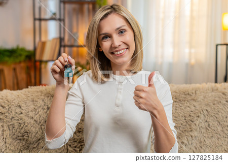 Adult woman celebrating new apartment at home, showing house keys proudly to camera with smile 127825184