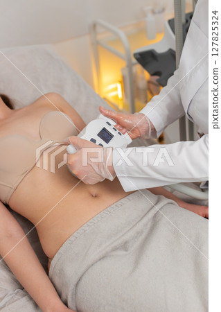 Caucasian woman receives abdomen vacuum massage from cosmetologist using LPG device in beauty clinic 127825324