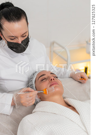Enzyme therapy, beautician applying moisturizing medical cream on young woman face with brushes Enzyme therapy, beautician applying moisturizing medical cream on young woman face with brushes 127825325