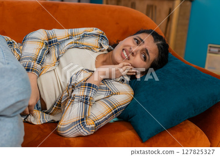 Indian woman holding cheek lying on sofa experiencing severe toothache pain discomfort distressed 127825327