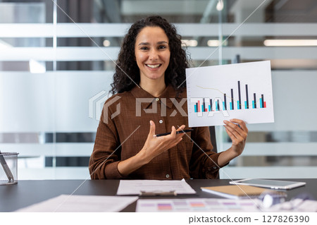 A smiling woman points to a graph during a presentation in an office setting. Business, data analysis. 127826390