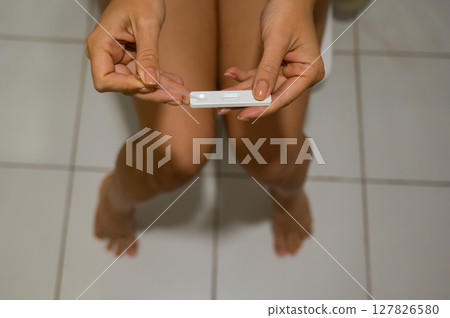 A woman takes an express pregnancy test while sitting on the toilet. 127826580