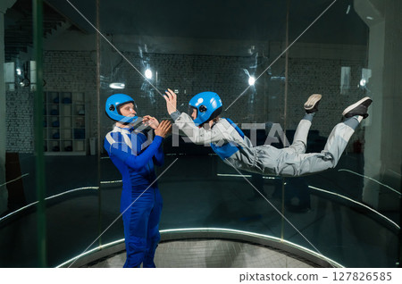 A male instructor teaches a woman how to fly in a wind tunnel. Free fall simulator. 127826585