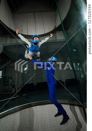 A male instructor teaches a woman how to fly in a wind tunnel. Free fall simulator. 127826594