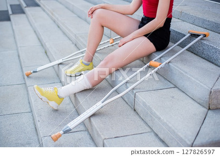 Girl with leg injury sits on the stairs with crutches. Girl with leg injury sits on the stairs with crutches. 127826597