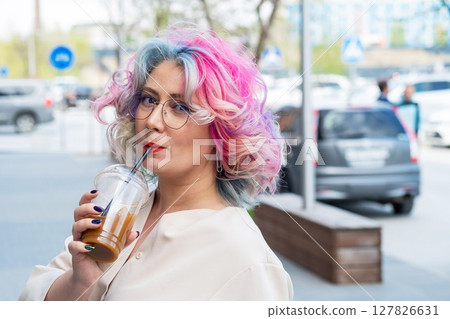 Close-up portrait of curly Caucasian woman with multi-colored hair wearing glasses. The hairstyle model is drinking a cold drink 127826631