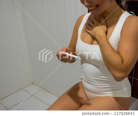 A woman takes an express pregnancy test while sitting on the toilet. 127826641