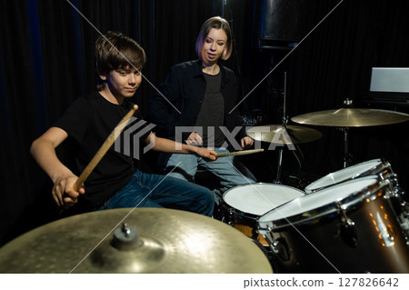 Young caucasian woman teaches a boy to play the drums in the studio on a black background. Music school student 127826642