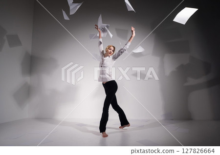 A graceful ballerina in a business suit throws documents. Business woman dance barefoot on a white background A graceful ballerina in a business suit throws documents. Business woman dance barefoot on a white background 127826664