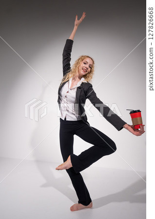 Barefoot ballerina in business suit dancing with a cup of coffee on a white background. Barefoot ballerina in business suit dancing with a cup of coffee on a white background. 127826668