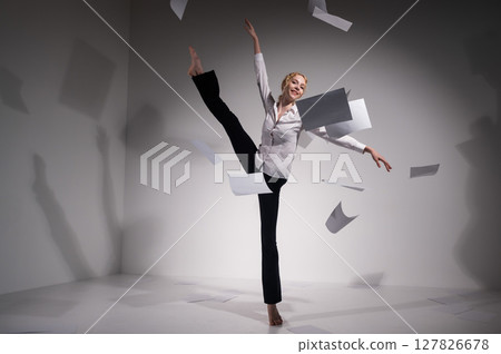 A graceful ballerina in a business suit throws documents. Business woman dance barefoot on a white background 127826678