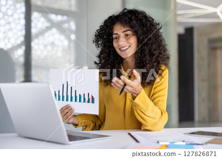 Businesswoman is presenting a financial report during an online conference in a bright office space, using graphs for clarity 127826871