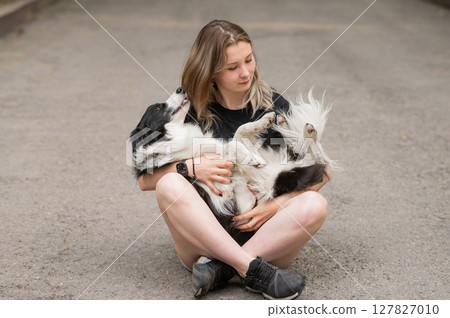 Young caucasian woman sitting on asphalt and hugging border collie dog.  127827010