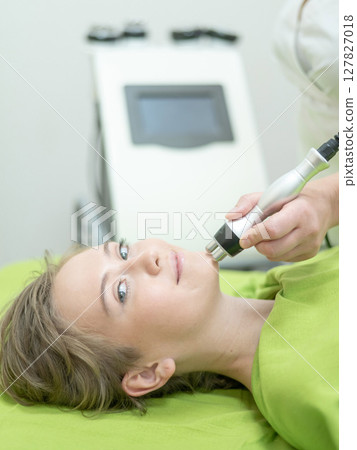 Caucasian woman undergoing radio wave RF lifting procedure in beauty salon. Caucasian woman undergoing radio wave RF lifting procedure in beauty salon. 127827018