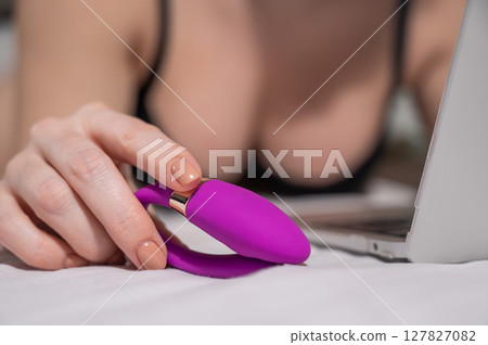 A woman lies on the bed and synchronizes the kegel machine with a laptop. 127827082