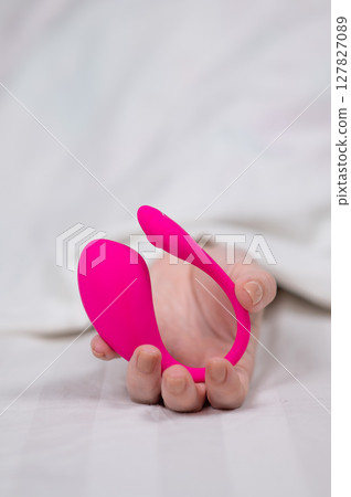 Woman holding curved pink vibrator while lying in bed.  127827089