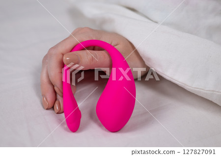 Woman holding curved pink vibrator while lying in bed.  127827091