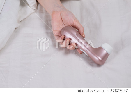 Woman lying in bed holding clitoral vacuum vibrator.  127827097