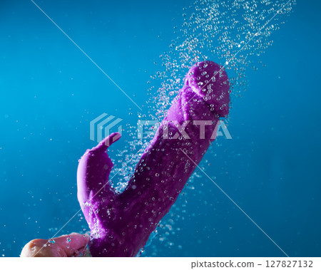 A woman washes a purple vibrator under the shower. Waterproof sex toy on a blue background. A woman washes a purple vibrator under the shower. Waterproof sex toy on a blue background. 127827132