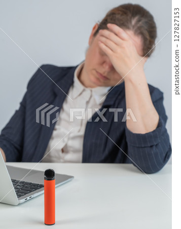 Caucasian businesswoman working on laptop. Disposable vape in foreground.  127827153