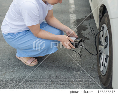 A woman pumps up a tire on a car.  127827217