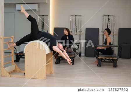 Three women doing Pilates on a reformer and a Pilates barrel.  127827230