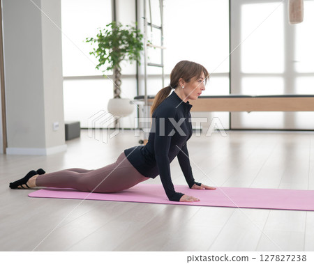 Concentrated woman doing pilates in studio alone. Concentrated woman doing pilates in studio alone. 127827238