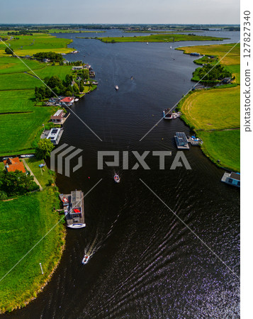 A top-down view of a marina with multiple boats docked along wooden piers, a boat cruising through a narrow waterway surrounded by green parks and natural grassy areas. 127827340