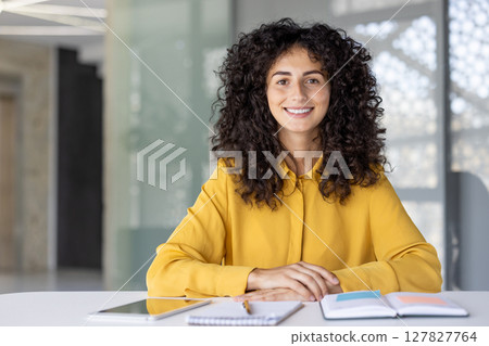 Confident Businesswoman Sitting at a Desk with Notebooks and Digital Tablet. Confident Businesswoman Sitting at a Desk with Notebooks and Digital Tablet. 127827764