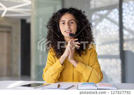Smiling woman wearing a headset during a video conference, seen from the first-person perspective, in a modern office setting Smiling woman wearing a headset during a video conference, seen from the first-person perspective, in a modern office setting 127827792