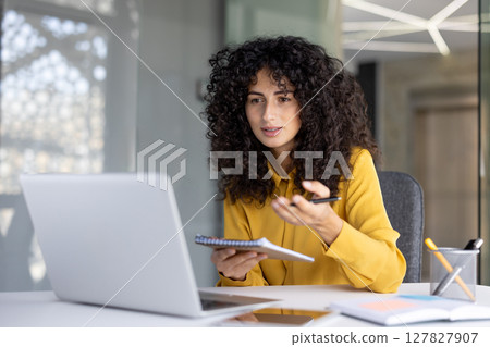 Successful woman with notebook in hands watching video course, online business meeting conference. Office worker uses laptop for video call, communicates with colleagues remotely. 127827907
